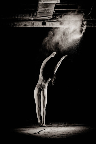 La chica con la harina en el cuerpo estira los brazos con harina tirada sobre fondo negro imagen en blanco y negro
 - Foto, imagen