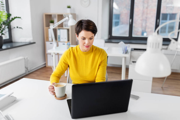 businesswoman with laptop drinks coffee at office - Φωτογραφία, εικόνα