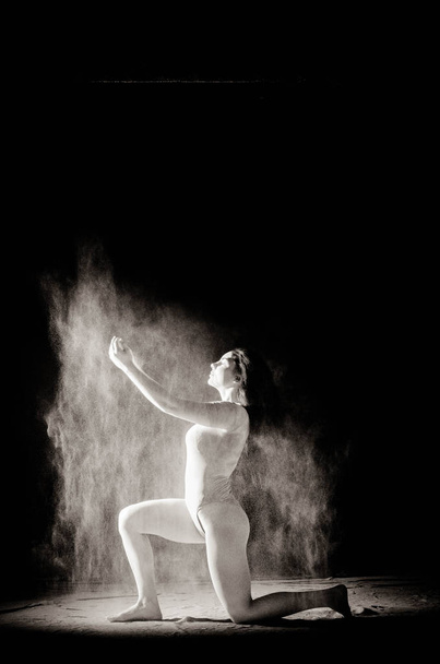 La chica con la harina en el cuerpo estira los brazos con harina tirada sobre fondo negro imagen en blanco y negro
 - Foto, imagen