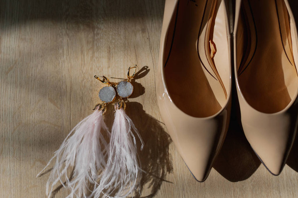 Beautiful womens shoes and gold earrings on the wooden floor in the sun. - Photo, Image