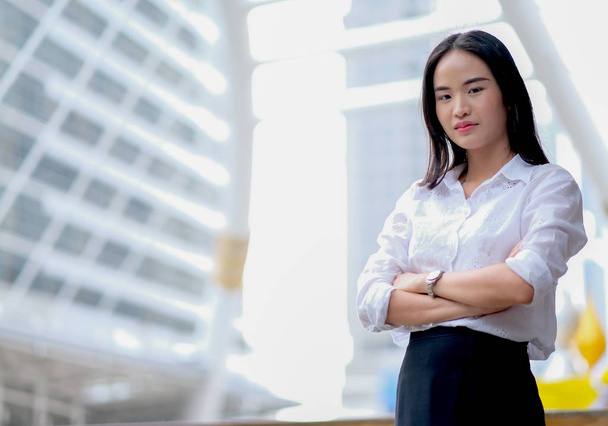 asiatische schöne Business-Girl mit weißem Hemd wirken so selbstbewusst und stehen zwischen hohen Gebäude in der Großstadt in der Tageszeit. - Foto, Bild