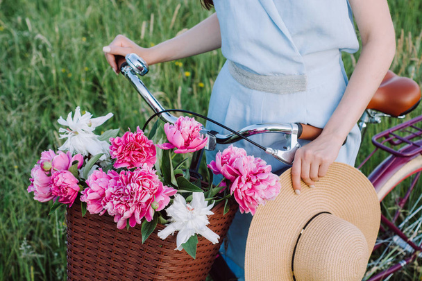 Closeup images of beautiful female hands hold a bicycle with a basket of red and white flowers and a stylish hat on the background of nature. Concept outdoor nature lifestyle. - Fotoğraf, Görsel