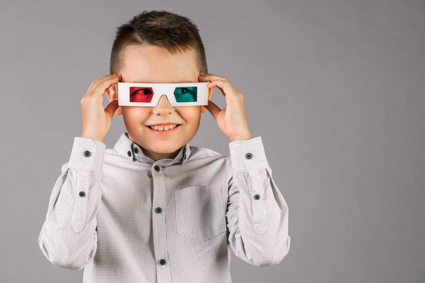 Νεαρό όμορφο αγόρι με 3D γυαλιά σε γκρίζο φόντο στο στούντιο. - Φωτογραφία, εικόνα