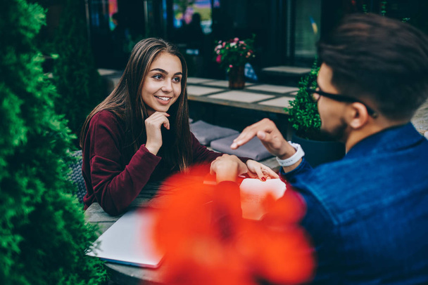 Cheerful brunette woman having positive conversation with male friend on meeting sitting at cafe terrace, hipster girl listening to interesting story of guy enjoying spending free time together - Zdjęcie, obraz