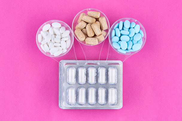 Värikkäitä pillereitä lasi- ja läpipainopakkauksissa, joissa kapselit vaaleanpunaisella pohjalla
 - Valokuva, kuva