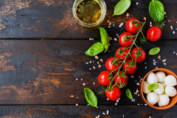 Fresh cherry tomatoes, basil leaves, mozzarella cheese and olive oil on old wooden background. Caprese salad ingredients. Selective focus. - Zdjęcie, obraz