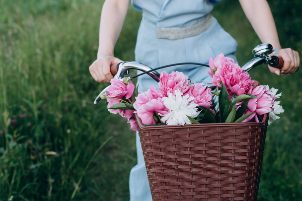 Close up shot of female hands, she holds a bicycle with a basket of red and white peonies flowers. Active vacation nature. summer concept - Foto, immagini