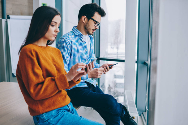 Millennial hipster girl and guy sitting together ignore real conversation prefere to chatting in social networks via modern smartphones and 4G internet connection, addiction to modern devices - Photo, image