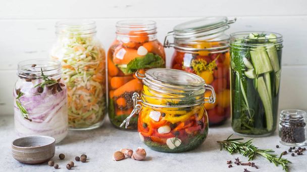 Marynowane warzywa. Solenie różnych warzyw w szklanych słoikach do długotrwałego przechowywania. Konserwuje warzywa w szklanych słoikach. Różnorodność sfermentowanych zielonych warzyw na stole - Zdjęcie, obraz