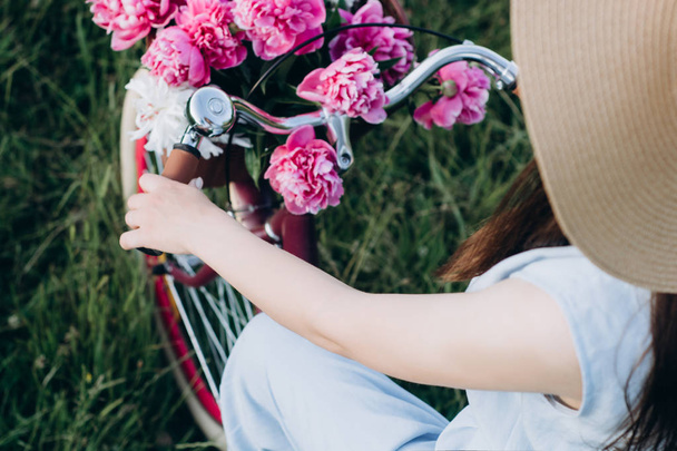 Foco seletivo menina bonita e jovem em um chapéu monta uma bicicleta com uma cesta de flores vermelhas e brancas no fundo da natureza. Conceito ao ar livre natureza estilo de vida
. - Foto, Imagem