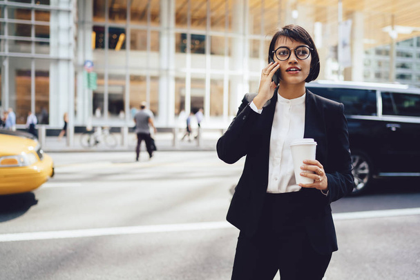 Young female boss calling to operator service for checking account balance during coffee break in downtown, woman in elegant suit using 4g connection on smartphone for communicate with partner - Photo, Image