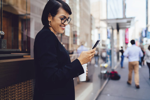 Cheerful female lawyer in stylish optical spectacles enjoying work break in downtown feeling good from received email with information about notification for application on smartphone gadget - Фото, зображення