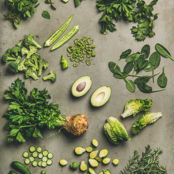Healthy vegan ingredients layout. Flat-lay of whole and cut green vegetables and herbs over concrete background, top view, square crop. Vegetarian, weight loss, raw, clean eating concept - Foto, Imagem