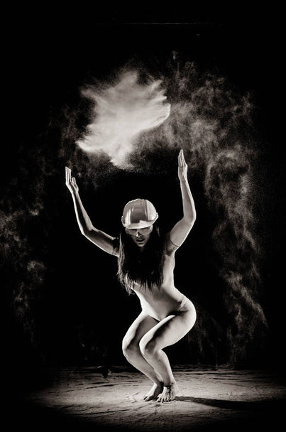 das Mädchen mit dem Mehl auf dem Körper streckt die Arme mit geworfen Mehl auf schwarzem Hintergrund Schwarz-Weiß-Bild - Foto, Bild
