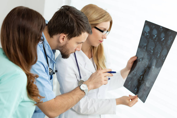 Handsome young doctor pointing at x-ray exam during medical consultation - Φωτογραφία, εικόνα