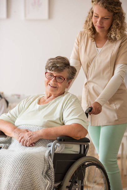 Positive senior patient on wheelchair with supportive nurse - Valokuva, kuva
