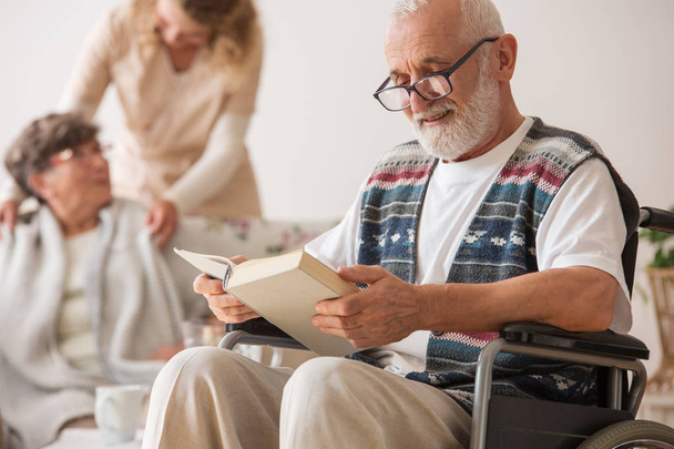Senior man on wheelchair reading a book - Фото, изображение