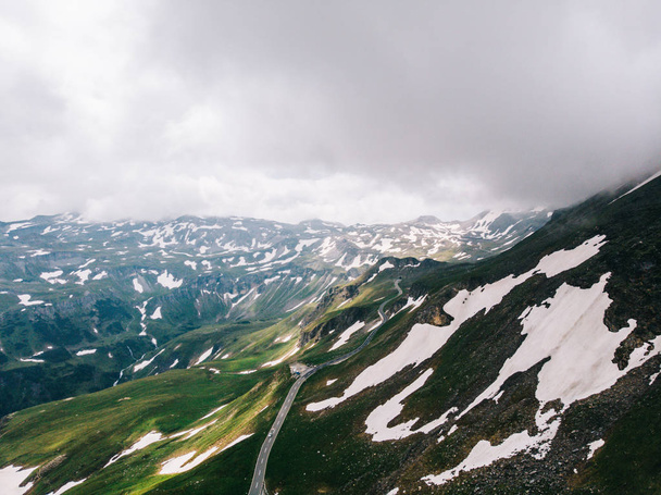 Bird's eye view of road in snowy mountains under cloudy sky. Aerial view of scenic route in Austria with name Grossglockner High Alpine Road. Hochtor Pass on high altitude with panoramic views - Photo, image