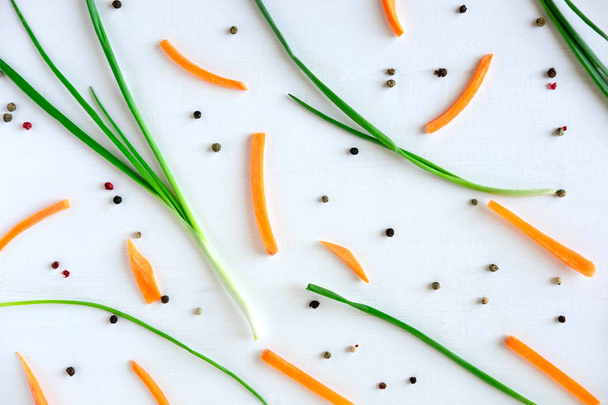 Culinary theme pattern with carrot pieces, green onions and seasonings on a white wooden background. View from above - Valokuva, kuva