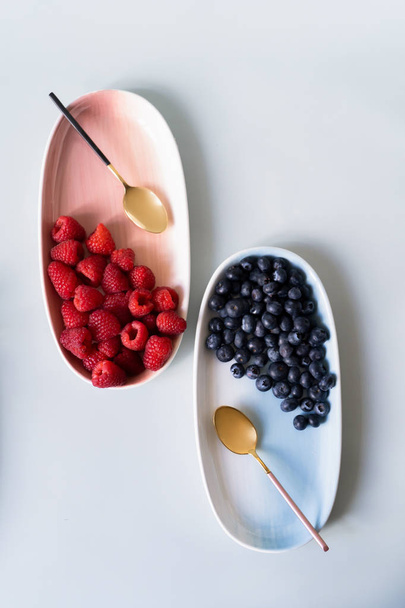 Summer berries blueberries, raspberries on the new elegant plates of pink, blue colors. New luxury Golden cutlery view from above on a isolated white background. Top view. - Foto, Imagem