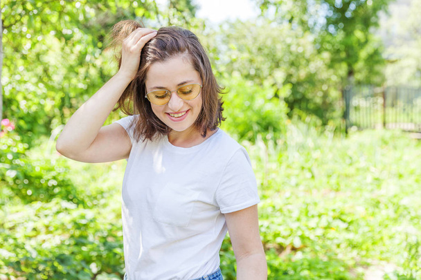 Happy girl smiling. Beauty portrait young happy positive laughing brunette woman in trendy yellow sunglasses on park or garden background - Photo, Image