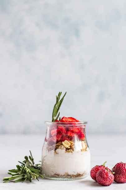 Breakfast with yogurt, granola and fresh strawberry in a mason jar on a light stone background. Healthy breakfast or dessert concept, selective focus. Copy space. - Foto, afbeelding