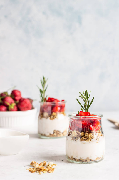 Breakfast with yogurt, granola and fresh strawberry in a mason jar on a light stone background. Healthy breakfast or dessert concept, selective focus. Copy space. - Фото, изображение