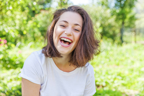 Boldog lány mosolyogva. Szépség portré fiatal boldog nevető barna nő a parkban vagy a kertben háttér - Fotó, kép