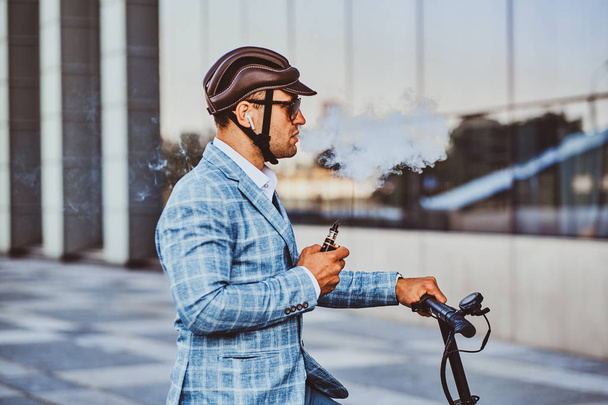 Eleganter Mann mit Elektroroller raucht Dampf - Foto, Bild