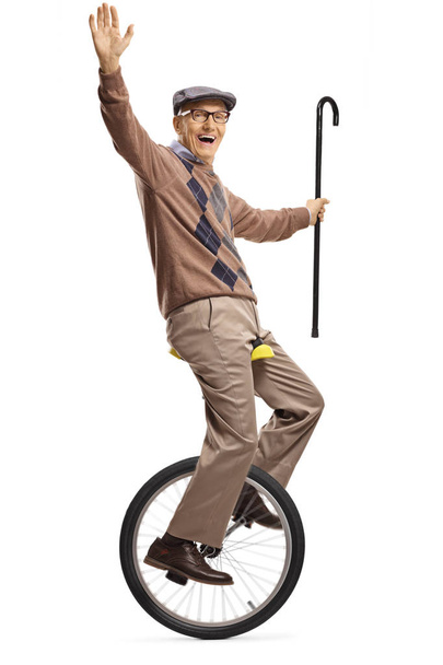Elderly man riding a unicycle and holding a cane up  - Foto, afbeelding