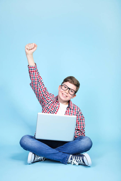 Young boy with a laptop sitting on blue background - Фото, изображение