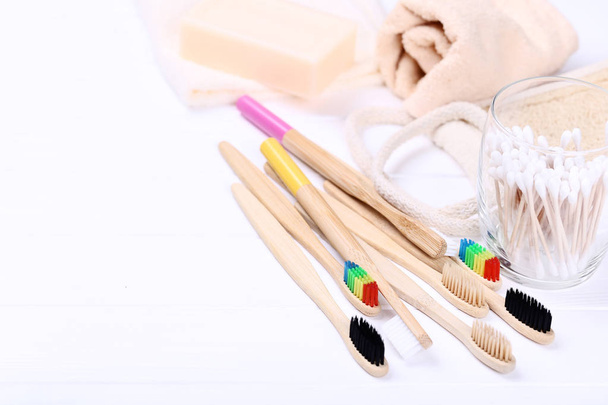 Bamboo toothbrushes with cotton sticks and washcloth on white wooden table - 写真・画像