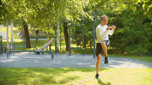 Atletyczny mężczyzna rozgrzewający nogi z podstawowymi ćwiczeniami w parku - Zdjęcie, obraz