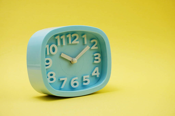 light blue alarm clock with space copy on yellow background - Foto, Imagen