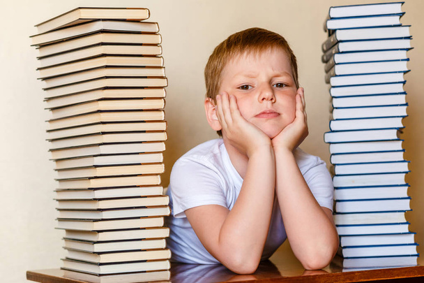 sad eight-year-old boy and a lot of books on the table - Фото, зображення