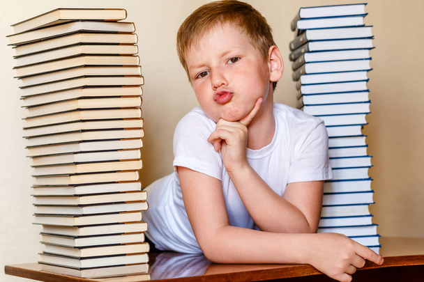 eight-year-old boy in a white t-shirt and a lot of books on the table - Фото, зображення