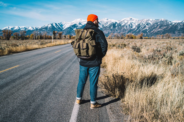 Tourist traveller with backpack standing into road in nature environment, back view of male hiker looking and enjoying breath of fresh clean air during trip to mountains, relax and holiday concept - Фото, изображение