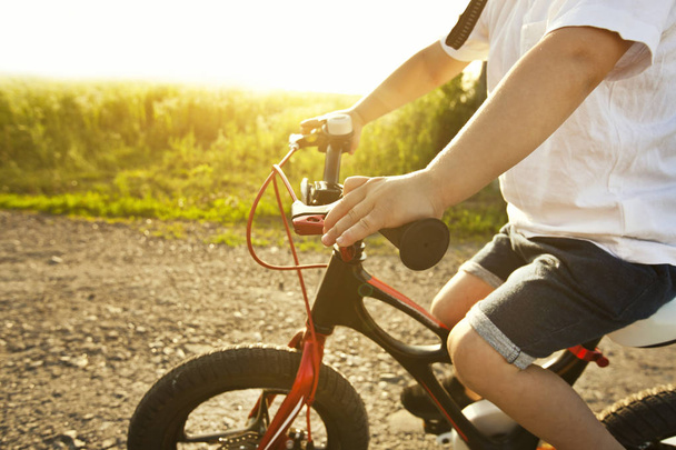 Pikkupoika ajaa polkupyörällä asfalttitien läpi illalla.
 - Valokuva, kuva