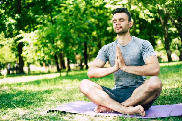 Male yoga relaxation. Sporty and slim handsome young man is doing yoga exercises in city park outdoors. Healthy lifestyle and strong soul and body - Фото, зображення