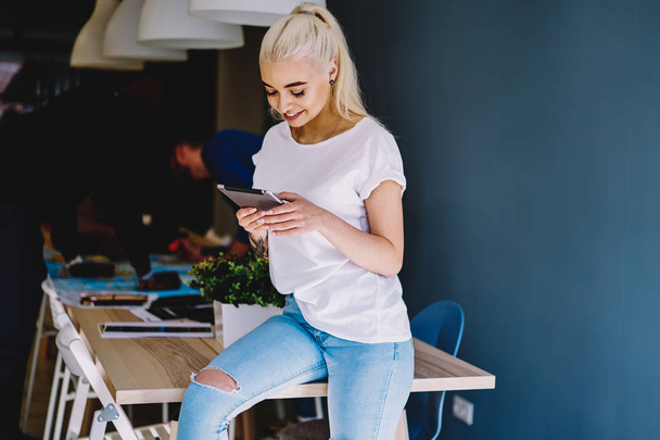 Pretty caucasian female student satisfied with installing new app on portable pc for learning, cheerful blonde millennial woman reading news from social networks on tablet during work brea - Foto, Bild