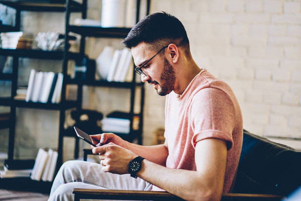 Handsome hipster guy dressed in casual look reading news on content website with information for freelance copywriters using free home internet on digital tablet during leisure time in loft apartment - Photo, Image
