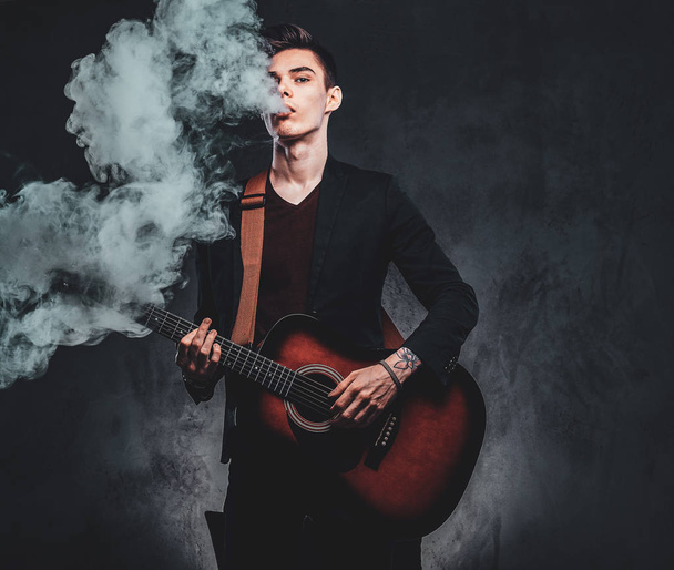 Cara atraente está tocando guitarra acústica e fumando
 - Foto, Imagem