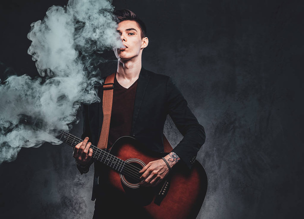Atraktivní chlap hraje na akustickou kytaru a kouří - Fotografie, Obrázek