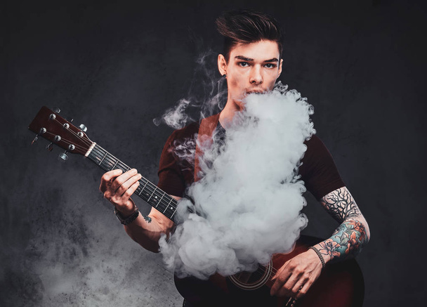 Attractive guy is playing acoustic guitar and smoking - Photo, Image