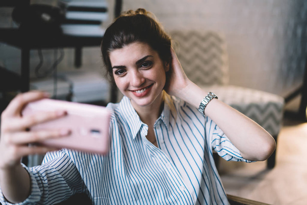 Attractive young woman making selfie on modern mobile phone to upload in social networks.Charming hipster girl smiling at front camera of digital smartphone and taking photo resting at home - Foto, Bild