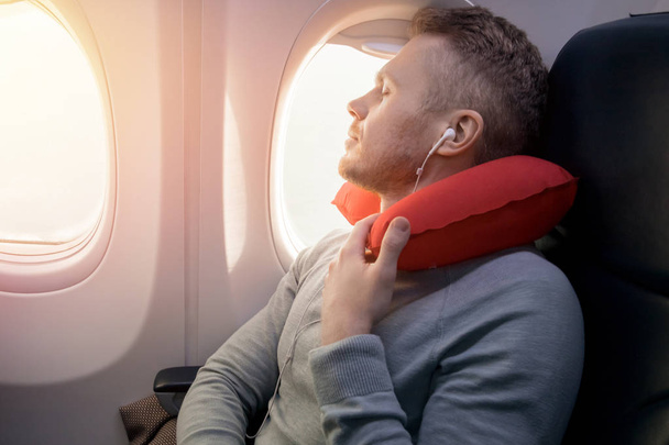 Male passenger of airplane listens to music and enjoys pillow for sleeping in chair. - Photo, Image