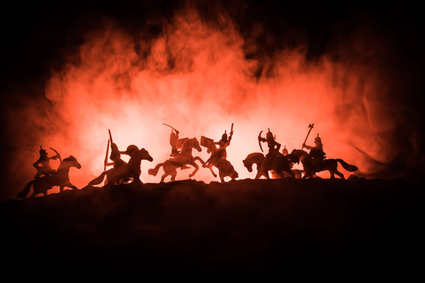 Medieval battle scene with cavalry and infantry. Silhouettes of figures as separate objects, fight between warriors on dark toned foggy background with medieval castle. - Photo, Image