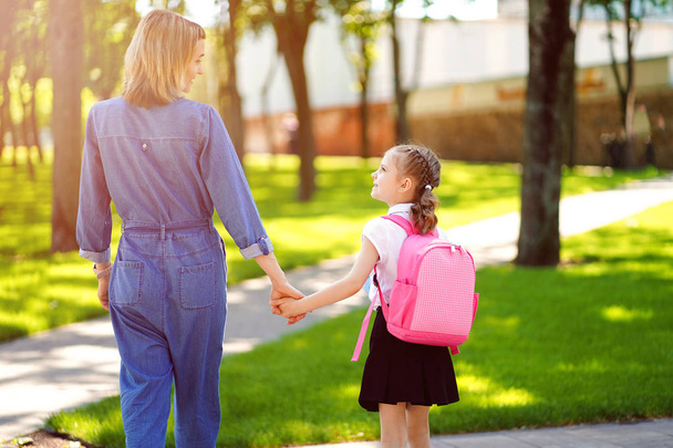Parent and pupil of primary school go hand in hand. Woman and girl with backpack behind the back. Beginning of lessons. First day of fall - Foto, Imagem