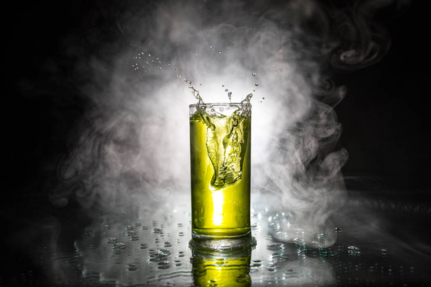 Bicchiere da cocktail spruzzato su sfondo fumé scuro o cocktail colorato in vetro. Intrattenimento da party club. Luce mista
. - Foto, immagini