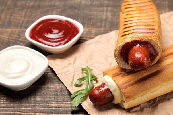 Francuskie Hot dogi. Smaczne Hot dogi na pokładzie i sos na brązowym drewnianym stole. Fast food Street Food. kiełbasy w kok. - Zdjęcie, obraz